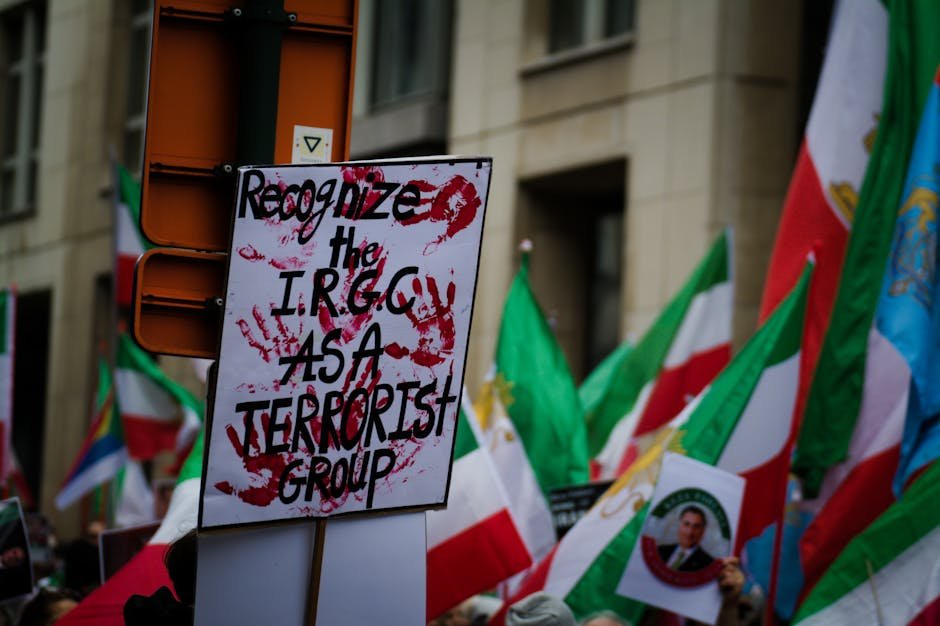 Bahrain Dismantles Spy Network Linked to Iran’s IRGC, Revokes Citizenship Protest in Brussels with flags and signs demanding IRGC recognition as a terrorist group.