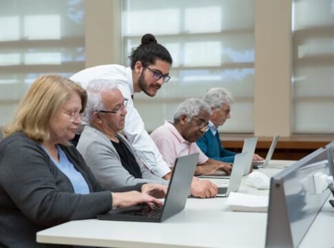 Senior adults use laptops in a classroom setting, guided by a young instructor. Senior adults use laptops in a classroom setting, guided by a young instructor.