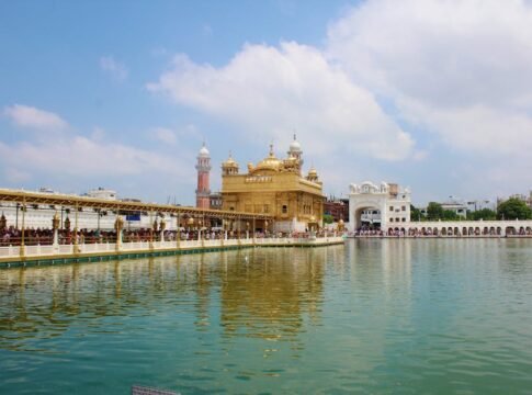 Serene view of the Golden Temple in Amritsar, India, with reflection on water under clear skies.