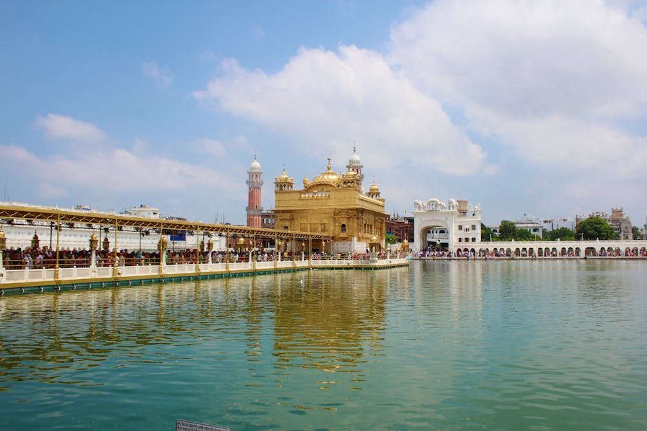 Serene view of the Golden Temple in Amritsar, India, with reflection on water under clear skies.