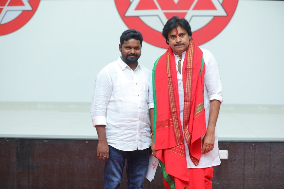 Andhra Pradesh Deputy CM Orders Urgent Action Plan for Godavari River Pollution Two Indian men indoors, one in traditional attire, with a logo background.