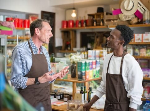 Two colleagues in aprons conversing in a grocery store setting.