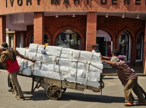 Two men exert effort pushing a heavy cart full of packages on an urban city street. Two men exert effort pushing a heavy cart full of packages on an urban city street.