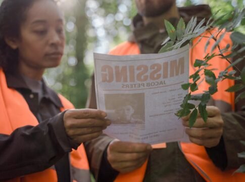 Volunteers in forest holding a missing person poster during search operation.