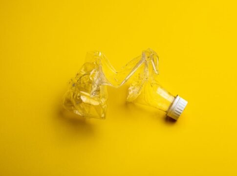 A crumpled plastic bottle against a bright yellow backdrop, highlighting recycling themes.