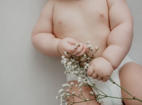 A cute baby gently holding delicate white flowers, symbolizing innocence and new life. A cute baby gently holding delicate white flowers, symbolizing innocence and new life.