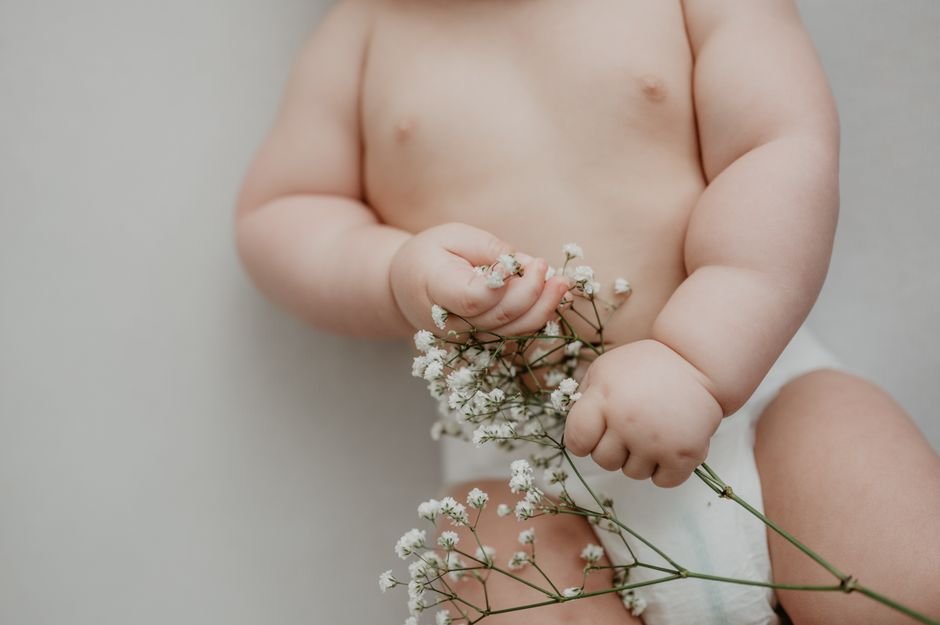 Bengaluru Newborn Undergoes Rare Heart Surgery After Parents’ Six-Year Wait for Twins A cute baby gently holding delicate white flowers, symbolizing innocence and new life.