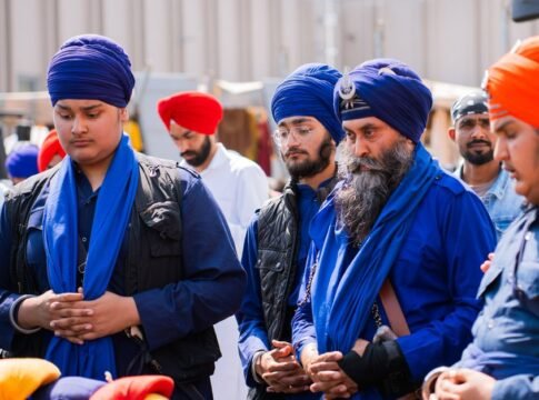 A group of Sikh men wearing traditional blue turbans participate in a peaceful assembly outdoors.