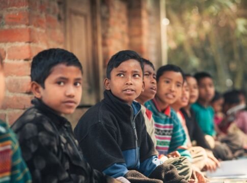 A group of children from Bangladesh sitting outdoors, engaged in learning at a rural school.