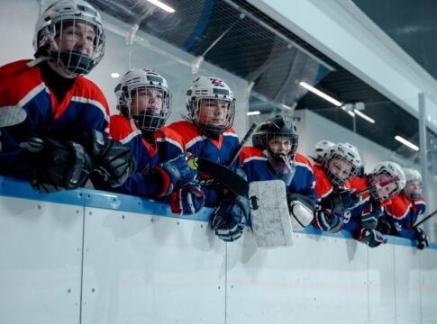 A junior ice hockey team waits eagerly at the rink edge, embodying teamwork and anticipation.
