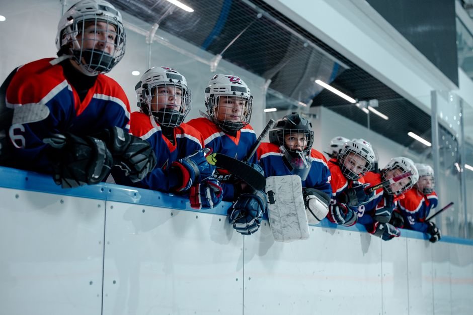A junior ice hockey team waits eagerly at the rink edge, embodying teamwork and anticipation.