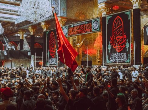 A large crowd participates in a religious ceremony at a notable landmark in Karbala, Iraq.