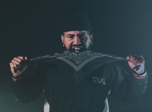A man intensely holding a patterned bandana in a dark, moody setting.