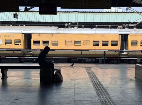 A person sitting on luggage at a train station platform with a yellow train in the background. A person sitting on luggage at a train station platform with a yellow train in the background.