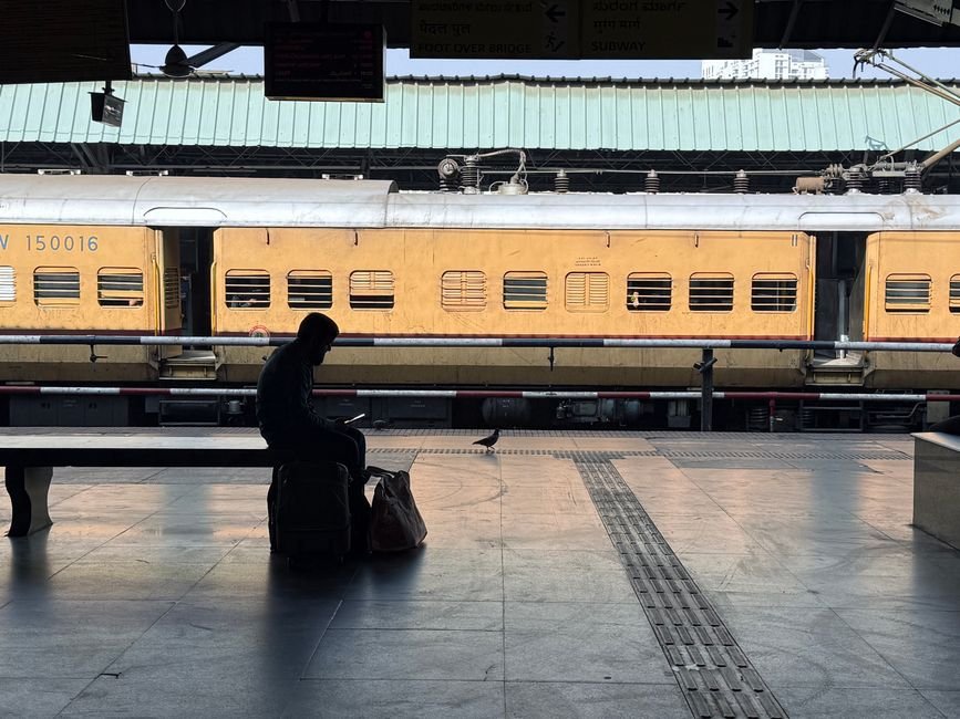 Pune Railway Station Faces Nine-Hour Block on Sunday, Disrupting Services A person sitting on luggage at a train station platform with a yellow train in the background.