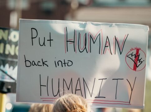 A protest sign with the message 'Put Human back into Humanity' during a daylight rally.