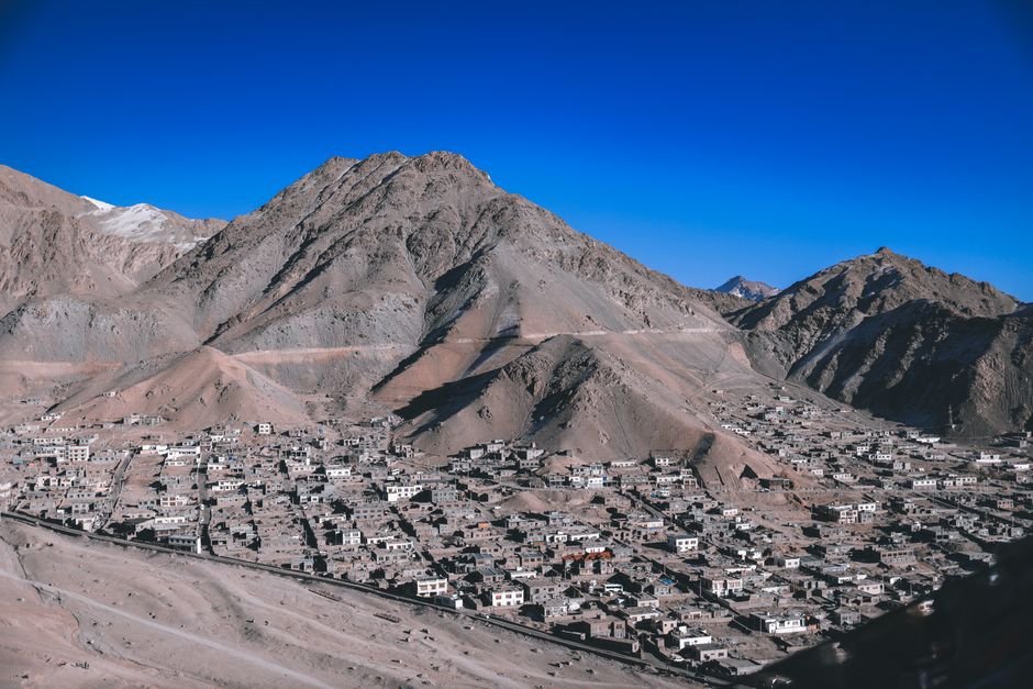 Ladakh Sees Over 43% Rise in Tourist Arrivals in First Five Months of 2026 A stunning aerial view of Leh with its rugged mountain backdrop and scattered village buildings under a clear blue sky.