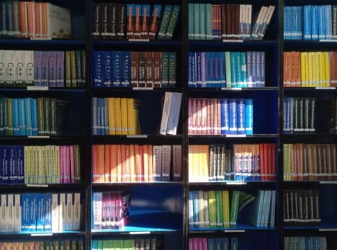 A vibrant library bookshelf displaying a range of educational books organized by subject.