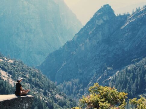 A woman practices meditation on a cliff edge, surrounded by majestic mountains and serene nature. A woman practices meditation on a cliff edge, surrounded by majestic mountains and serene nature.