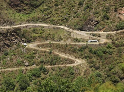 Aerial view of a winding rural road through lush green mountains in Lapas, India.