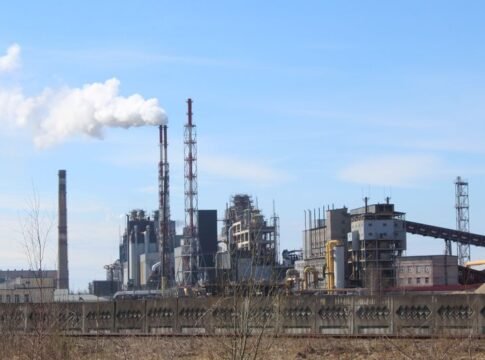 An industrial factory with smoke emissions against a clear blue sky. An industrial factory with smoke emissions against a clear blue sky.