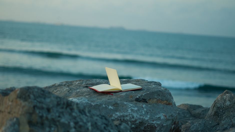 Journal of Coastal Research Focuses on Diverse Coastal Studies, Including Erosion and AI Applications An open notebook rests on a rock by the sea, capturing the serenity of the coastal landscape at sunset.