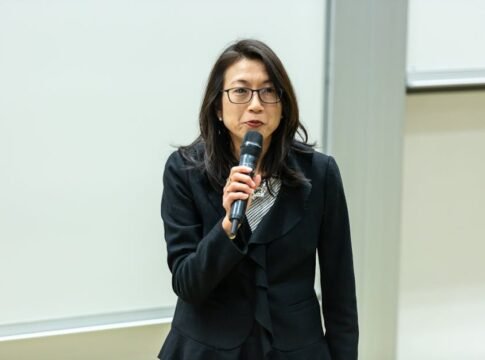 Asian woman in a professional attire giving a talk in a conference room.