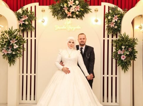 Beautiful couple in elegant wedding attire surrounded by floral decor indoors.