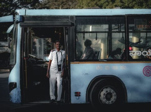 Bus driver wearing a white uniform standing by the bus door, sunlight casting shadows inside Bus driver wearing a white uniform standing by the bus door, sunlight casting shadows inside
