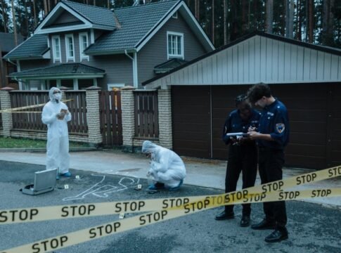 Forensic team investigates suburban crime scene with police officers and evidence markers.