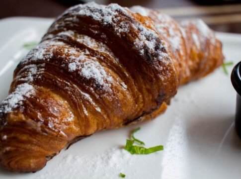 Freshly baked croissant dusted with powdered sugar, presented on a plate with mint garnish. Freshly baked croissant dusted with powdered sugar, presented on a plate with mint garnish.