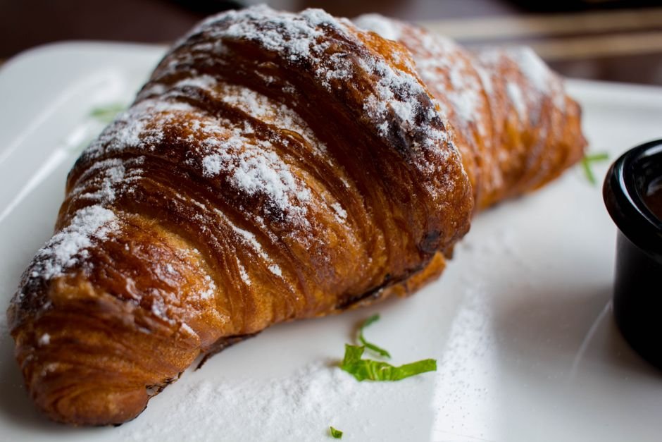 Pune Engineer Reimagines Croissants, Launches Unique Cafe Concept Freshly baked croissant dusted with powdered sugar, presented on a plate with mint garnish.