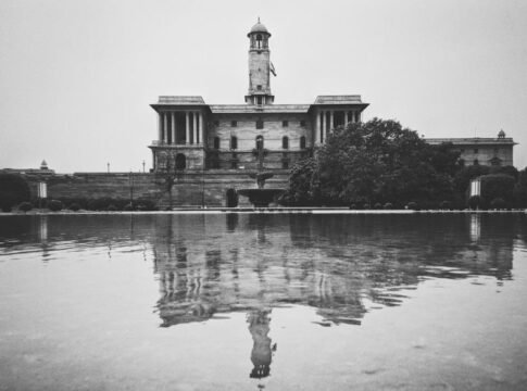 Grayscale photo of a historic building reflecting on water in New Delhi.