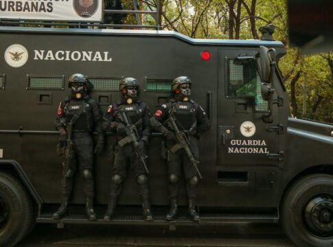 Guardia Nacional officers in tactical gear stand alert beside an armored vehicle.