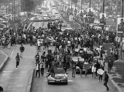 High angle view of a large protest on a busy city street with traffic congestion.