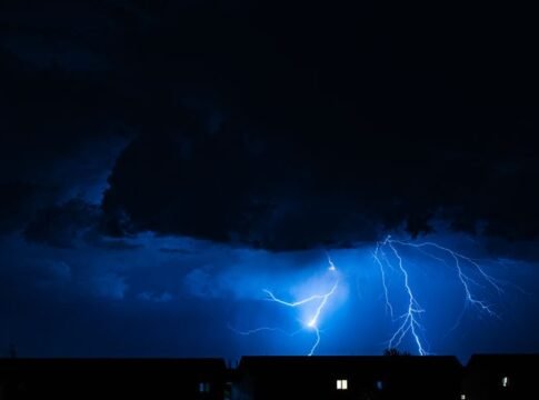Powerful lightning illuminates the night sky during a storm, casting silhouettes over city rooftops. Powerful lightning illuminates the night sky during a storm, casting silhouettes over city rooftops.