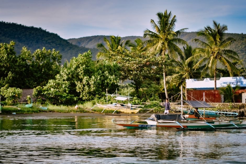Southern Philippines Hit by 7.8 Magnitude Earthquake, Four Dead and Tsunami Reported Scenic view of tropical harbor with traditional boats and lush greenery under a clear sky.