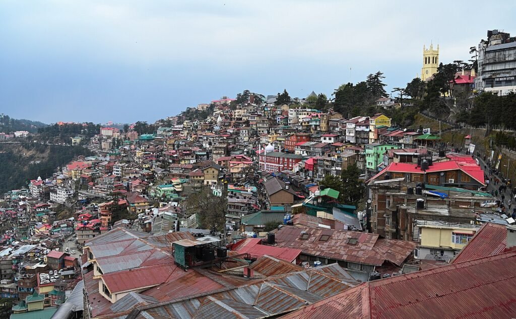 The image contains A view of the famous Christ Church in Shimla along with a cityscape of Shimla.on a cloudy day.