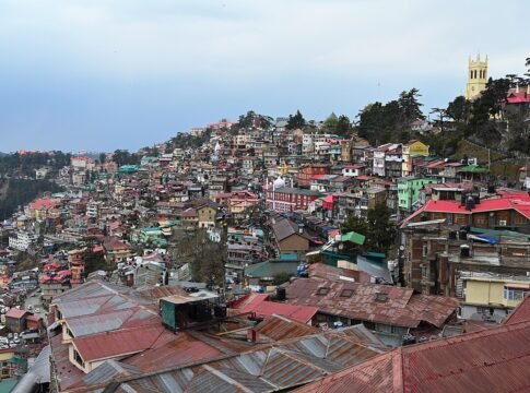 The image contains A view of the famous Christ Church in Shimla along with a cityscape of Shimla.on a cloudy day.