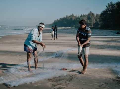 Two fishermen casting nets on a tranquil beach during the day. Perfect for lifestyle and travel themes.