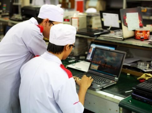 Two technicians in uniforms working on laptops in a laboratory setting. Focus on teamwork and technology.
