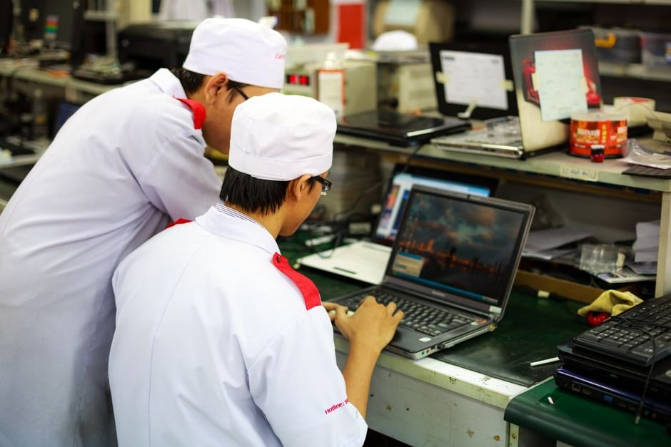 Foxconn Infuses ₹350 Crore into Indian Arm, Bolstering iPhone Production Two technicians in uniforms working on laptops in a laboratory setting. Focus on teamwork and technology.