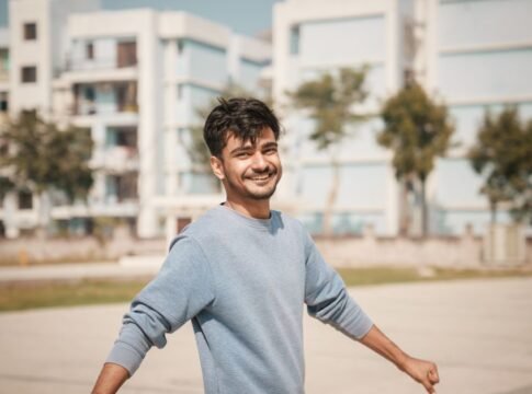 Young man outdoors with a smile, wearing a blue sweater with buildings in the background. Young man outdoors with a smile, wearing a blue sweater with buildings in the background.
