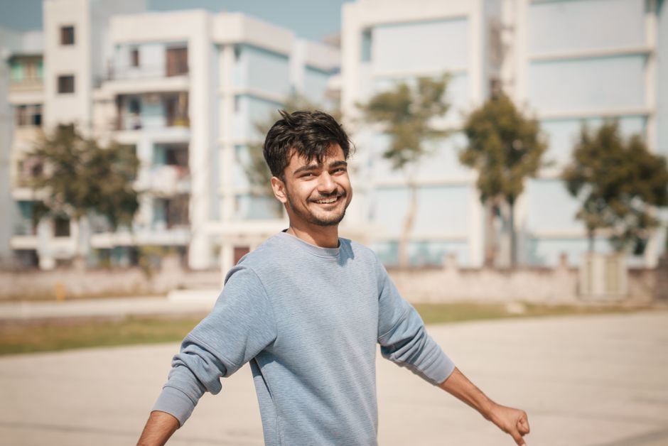 From UPSC Aspirant to Berry Farmer: A Satara Man’s Journey of Resilience Young man outdoors with a smile, wearing a blue sweater with buildings in the background.