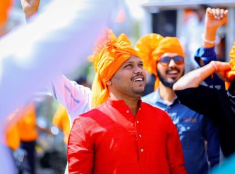 A joyful group of men celebrating outdoors in Malegaon, India, wearing bright turbans.