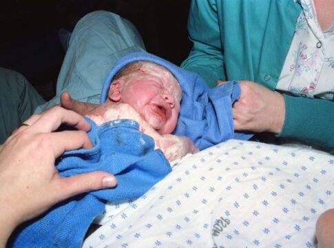 A newborn baby immediately after birth being wrapped in a hospital delivery room. A newborn baby immediately after birth being wrapped in a hospital delivery room.