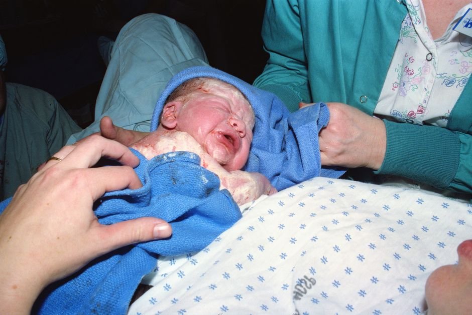 Men Sue North Dakota Hospital Alleging Birth Switch, Loss of Lifetimes A newborn baby immediately after birth being wrapped in a hospital delivery room.