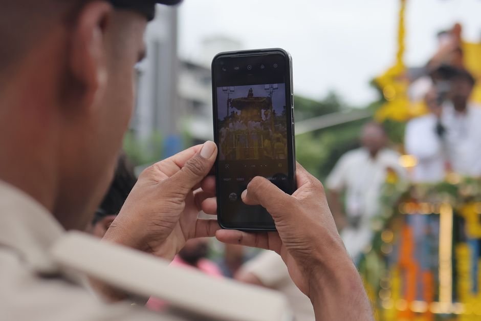 Jammu Police Debunks False Claims of Amarnath Yatra Pilgrim Deaths A person photographs the colorful Jagannath Rath Yatra parade with a smartphone.