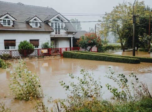A suburban house surrounded by floodwaters after heavy rain, showing impact of natural disaster. A suburban house surrounded by floodwaters after heavy rain, showing impact of natural disaster.