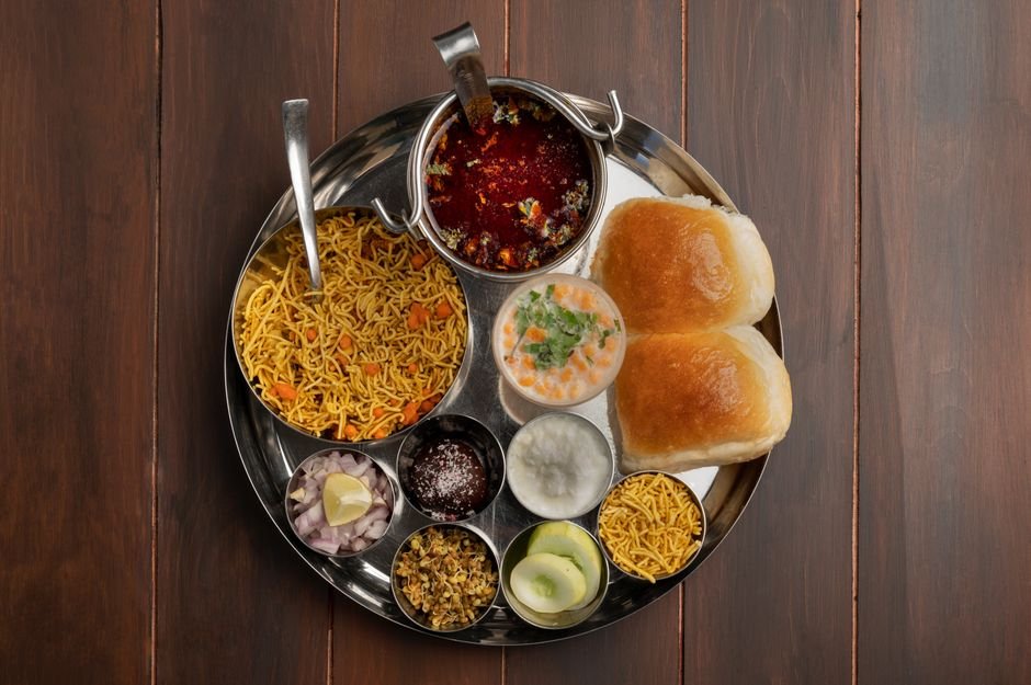 Pune’s Culinary Gems: Five Beloved Eateries Thriving Beyond Social Media Trends A top view of a traditional Maharashtra thali featuring spicy pav bhaji, vegetables, and condiments in Pune, India.